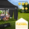 A family is sitting under a black pop-up canopy tent in a grassy outdoor setting. Produktbild-Vorschau