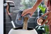 A person is emptying the dustbin of a cordless vacuum cleaner into a white bin. Produktbild-Vorschau