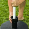 A person is inserting a white pole into a black base on a grassy lawn. Voir les images du produit