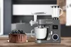 A kitchen appliance with a meat grinder and blender attachment, alongside a chocolate cake topped with berries, is displayed on a wooden table. Produktbild-Vorschau