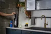 A person's hand is shown operating a SodaStream machine in a modern kitchen setting. Produktbild-Vorschau