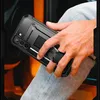 A person's hand holding a black phone case with a built-in stand and ring. Náhled obrázku produktu