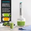 A hand blender with a beaker of green smoothie, a glass of smoothie, and ingredients like blueberries, avocados, and cucumbers. Produktbild-Vorschau