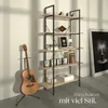 A guitar stands next to a bookshelf in a room with a large framed picture on the wall. Náhled obrázku produktu