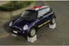 A blue Mini Cooper car with a Union Jack on the roof is parked on blocks on a street. Náhled obrázku produktu