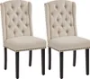 Two beige upholstered dining chairs with dark wood legs and nailhead trim are shown against a white background. Podgląd zdjęcia produktu