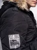Close-up of a person wearing a black hooded winter jacket with a fur-lined hood. A patch with the Lonsdale logo is visible on the sleeve. Náhled obrázku produktu