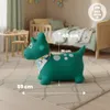 A green inflatable dinosaur toy is shown in a child's bedroom, placed on a rug in front of a bed. Podgląd zdjęcia produktu