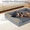 A Rottweiler puppy is sleeping on a gray dog bed next to a couch. Produktbild-Vorschau