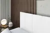 A close-up view of a bed with a white headboard, a bedside table with a lamp and a vase. Produktbild-Vorschau