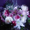 A close-up of a bouquet of artificial flowers intertwined with a string of white LED lights. Produktbild-Vorschau
