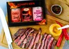 A gift box of spicy mustards is displayed next to a sliced steak, with chili peppers and a jar of mustard. Produktbild-Vorschau