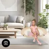 A young girl in a ballet outfit sits on a beige nest swing in a living room with a sofa and plants. Produktbild-Vorschau