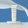 A tube of sunscreen is displayed on a white pedestal against a blue background with white wavy fabric. Produktbild-Vorschau