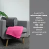 A pink fleece blanket is draped over a gray armchair, with a dark gray cushion behind it and a green plant leaf visible to the left. Text is overlaid on the right side of the image. Náhľad obrázku produktu