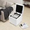 A white storage ottoman is open, revealing a book and a small stuffed animal inside. It is placed on a beige carpet next to a sofa with a black and white patterned throw blanket. Podgląd zdjęcia produktu