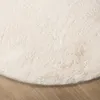 A close-up view of a round, fluffy rug in a cream color with beige accents, placed on a wooden floor. Produktbild-Vorschau