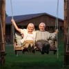 An elderly couple sitting on a swing in front of a house. Podgląd zdjęcia produktu