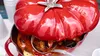 A close-up shot of a red Staub cocotte in the shape of a tomato, filled with food and being served with a ladle. Náhľad obrázku produktu