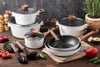 A collection of white cookware with wood-toned handles and lids, arranged on a wooden surface with various kitchen ingredients and utensils. Produktbild-Vorschau