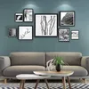 A collection of black and white framed pictures displayed on a teal wall above a gray sofa. Produktbild-Vorschau