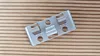 A metal mounting clip is placed on a wooden surface. Produktbild-Vorschau