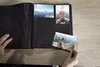 A person is placing a photo into a photo album on a wooden table. Anteprima dell’immagine prodotto