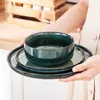 A person holding a stack of green ceramic plates and bowls. Náhled obrázku produktu