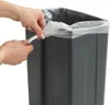 Hands are shown twisting the top of a clear plastic trash bag to tie it off, with a gray trash can visible in the background. Anteprima dell’immagine prodotto