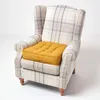 A yellow cushion sits on a plaid armchair. Náhled obrázku produktu