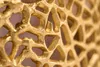 A close-up, detailed view of a golden, intricate metal structure. Produktbild-Vorschau