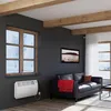 A living room with a black leather sofa, a red blanket, a window showing a snowy landscape, and a white electric heater mounted on the wall. Produktbild-Vorschau