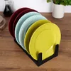 A set of colorful plates is displayed in a black plate stand on a wooden surface. Produktbild-Vorschau