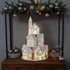 A decorative Christmas village scene displayed on a wooden dresser, framed by a garland of pine branches and ornaments. Produktbild-Vorschau