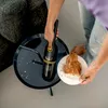 A person is using a handheld vacuum cleaner to clean up crumbs from a table next to a plate of food. Produktbild-Vorschau