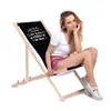 A woman sitting on a black deck chair with text on it. Produktbild-Vorschau