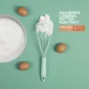 A kitchen whisk with whipped egg whites, eggs, and a bowl of whipped cream on a green background. Anteprima dell’immagine prodotto