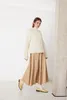 A woman is posing in a studio setting, wearing a white sweater and a beige skirt. Produktbild-Vorschau