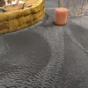 A close-up of a textured gray rug with a yellow pouf in the background. Voir les images du produit