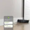A robot vacuum cleaner is shown next to a wall and a door, with a smartphone displaying app notifications in the foreground. Voir les images du produit