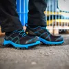 A person wearing black work pants and black and blue safety shoes. Náhľad obrázku produktu