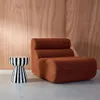A brown upholstered chair and a black and white striped side table are placed on a light gray floor against a wood-paneled wall. Produktbild-Vorschau