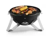 A black charcoal grill with food cooking on it, set against a white background. Produktbild-Vorschau