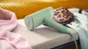 A mint green garment steamer lies on a fabric surface next to a pink garment and a leopard print pouch. Produktbild-Vorschau