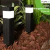 Two black solar garden lights with white tops are placed in a garden bed with mulch and plants. Náhled obrázku produktu