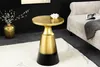 A gold and black accent table with a decorative lotus flower on top, placed on a rug next to a sofa. Produktbild-Vorschau