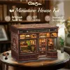 A miniature model of a coffee shop, displayed on a table with a blurred background of bookshelves. Náhled obrázku produktu