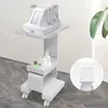 A white beauty trolley with a device on top and bottles on a lower shelf, set against a light gray wall and wooden floor. Podgląd zdjęcia produktu