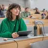 A woman in a lecture hall using a tablet and a power bank. Produktbild-Vorschau