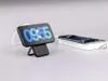 A smartphone is displayed on a charging stand, showing the time on its screen. Another smartphone is placed on a book in the background. Podgląd zdjęcia produktu